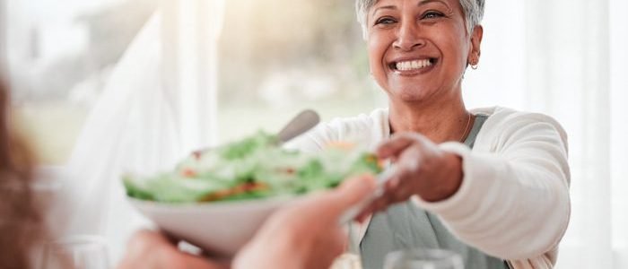 Family dinner, senior woman and healthy salad of a happy female with food in a home. Celebration, together and people with unity from eating at table with happiness and a smile in a house giving meal.