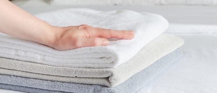 woman puts fresh clean towels on the bed in a hotel guest room, close-up. Woman's hand touches soft terry towels after cleaning the room